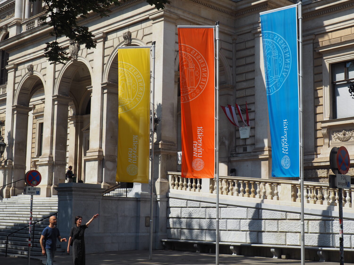 drei Fahnen vor der Universität Wien, unter denen zwei Menschen durchgehen