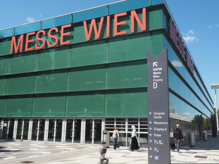 OLYMPUS DIGITAL CAMERA Das Gebäude der Messe Wien mit Schriftzug von vorne, darunter gehen drei Menschen